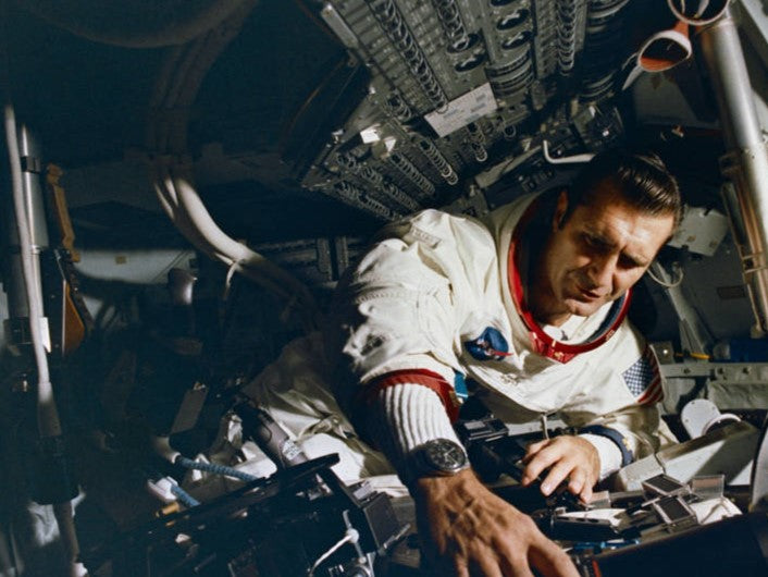 Astronaut inside a spacecraft cabin with equipment and control panels.